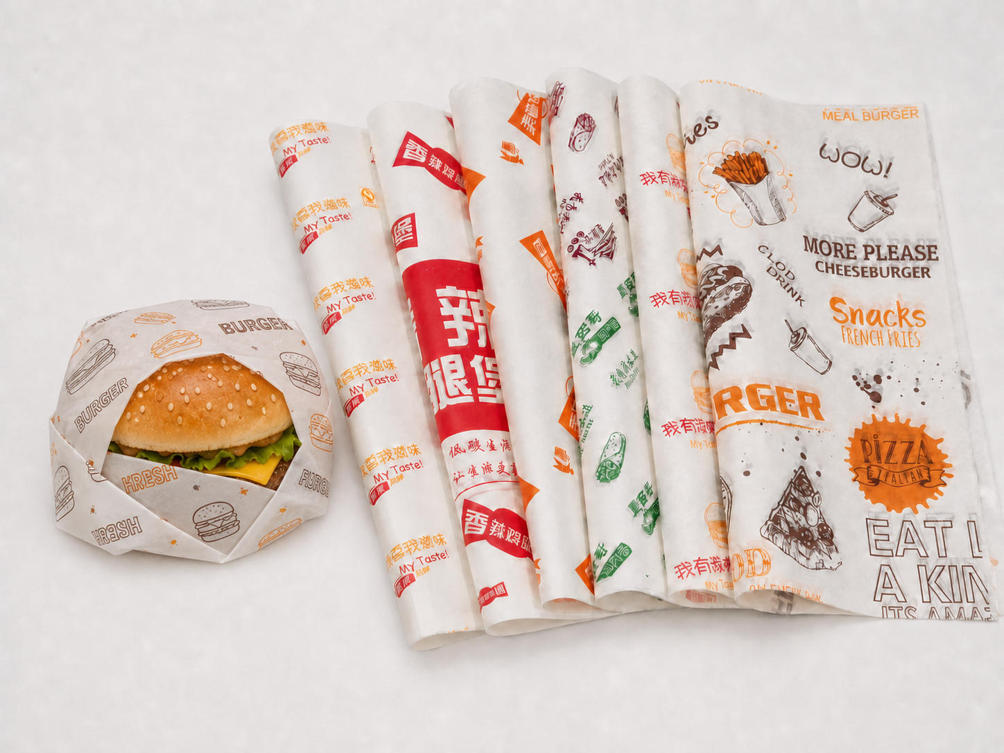 Burger wrapped in custom printed greaseproof paper beside a range of printed sheets